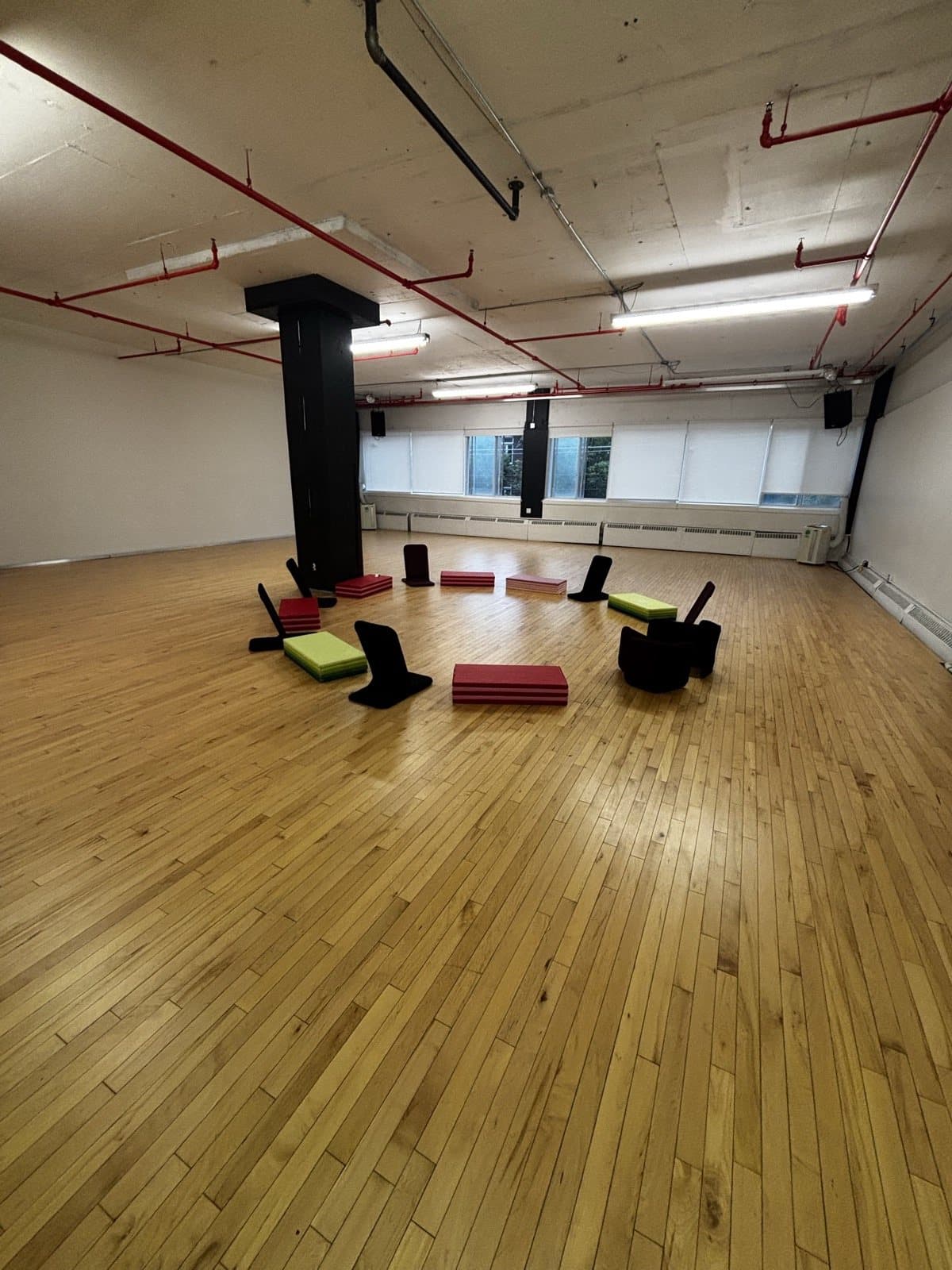 Des coussins et des chaises au sol disposés en cercle dans une grande salle aux planchers de bois